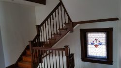 Interior of a house showing a wooden staircase with a stained glass window featuring a floral design on the right.